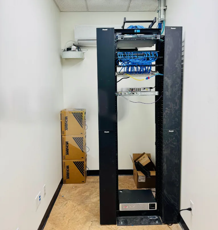 After: an open network rack with patch panels and blue cabling now stands in the same equipment room
